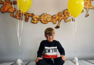 Chłopiec siedzi na tle fotograficznym i pozuje do zdjęcia wśród balonów